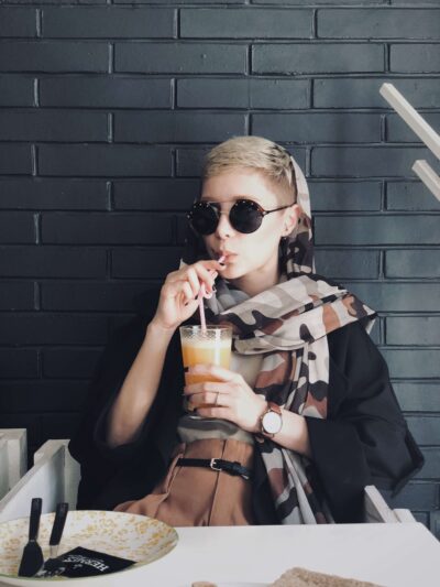 Woman looking in camera with sunglasses and pixie cut enjoying a drink